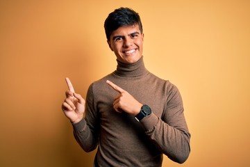 Poster - Young handsome man wearing casual turtleneck sweater over isolated yellow background smiling and looking at the camera pointing with two hands and fingers to the side.