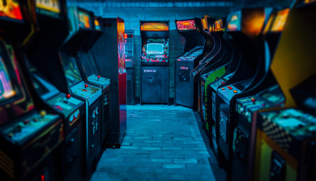 arcade video games in an empty dark gaming room with purple light with glowing vintage displays and 