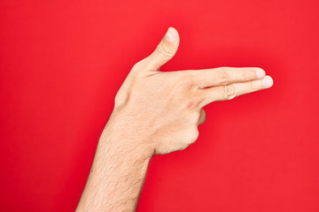 Hand of caucasian young man showing fingers over isolated red background gesturing fire gun weapon with fingers, aiming shoot symbol