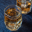 Two glasses of whiskey with ice on a blue background