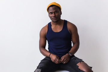 Wall Mural - Portrait of sexy trendy african man sitting on a chair on white background. Youth concept.