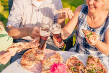 Cropped Image Of Happy People Eating Pizza And Toasting With Beer Outdoors On Sunset - Family Concept (focus On Glasses)