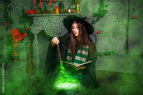 Fotomural A young witch in a black hat and mantle makes a potion in a black cauldron with a magic wand and a book