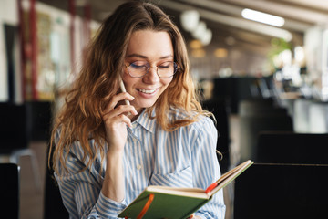 Canvas Print - Image of cheerful young woman talking on cellphone and holding planner