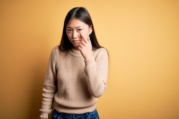 Wall Mural - Young beautiful asian woman wearing casual sweater over yellow isolated background Pointing to the eye watching you gesture, suspicious expression