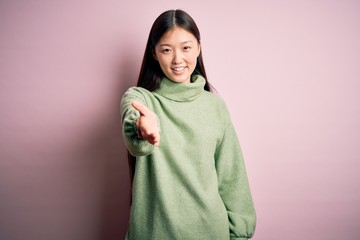 Sticker - Young beautiful asian woman wearing green winter sweater over pink solated background smiling cheerful offering palm hand giving assistance and acceptance.