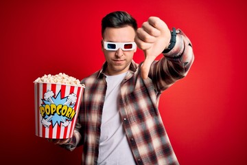 Wall Mural - Young handsome caucasian man wearing 3d movie glasses and eating popcorn looking unhappy and angry showing rejection and negative with thumbs down gesture. Bad expression.