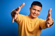 © Krakenimages.com - Young handsome latin man wearing yellow casual sweater over isolated blue background looking at the camera smiling with open arms for hug. Cheerful expression embracing happiness.
