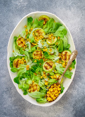 Wall Mural - Delicious fresh lettuce salad with grilled zucchini, corn and soft goat cheese with spices and olive oil. Selective focus, top view