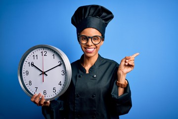 Wall Mural - African american baker woman wearing cooker uniform and hat doing countdown using clock very happy pointing with hand and finger to the side