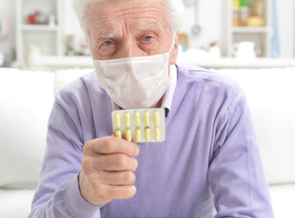 Sticker - Portrait of sad sick senior man with facial mask holding pills