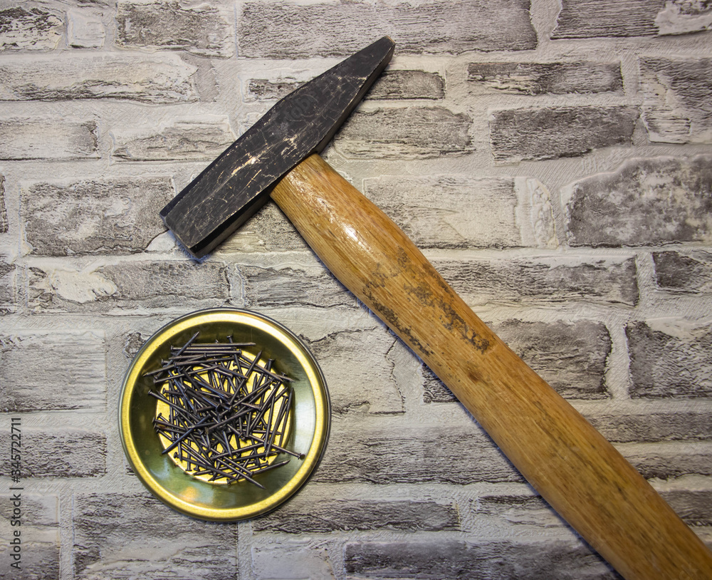 Black nails on a metal stand with a hammer on a brick wall background ...