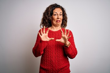 Poster - Middle age brunette woman wearing casual sweater standing over isolated white background afraid and terrified with fear expression stop gesture with hands, shouting in shock. Panic concept.