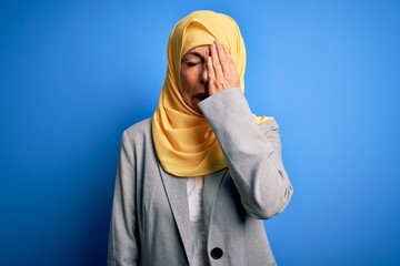 Wall Mural - Middle age brunette business woman wearing muslim traditional hijab over blue background Yawning tired covering half face, eye and mouth with hand. Face hurts in pain.