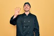 © Krakenimages.com - Young handsome cooker man with blue eyes wearing uniform and hat over yellow background showing and pointing up with fingers number four while smiling confident and happy.
