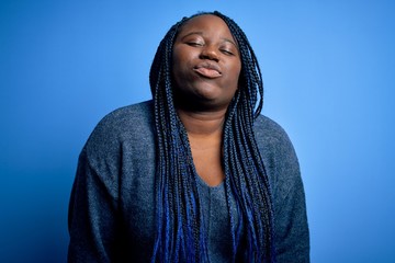 Poster - African american plus size woman with braids wearing casual sweater over blue background looking at the camera blowing a kiss on air being lovely and sexy. Love expression.