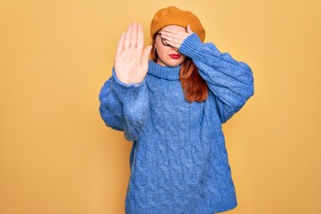 Canvas Print - Young beautiful redhead woman wearing french beret and glasses over yellow background covering eyes with hands and doing stop gesture with sad and fear expression. Embarrassed and negative concept.