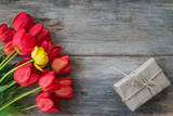 Fototapeta Tulipany - Bunch of red tulips and handmade gift box on old wooden background. Space for text, flat lay