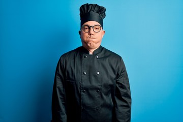 Poster - Middle age handsome grey-haired chef man wearing cooker uniform and hat puffing cheeks with funny face. Mouth inflated with air, crazy expression.