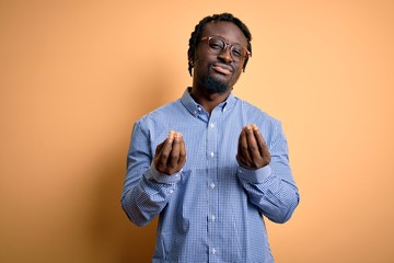 Poster - Young handsome african american man wearing shirt and glasses over yellow background doing money gesture with hands, asking for salary payment, millionaire business