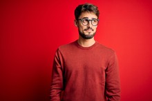 Young Handsome Man With Beard Wearing Glasses And Sweater Standing Over Red Background Smiling Looking To The Side And Staring Away Thinking.