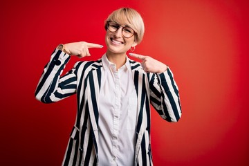 Sticker - Blonde business woman with short hair wearing glasses and striped jacket over red background smiling cheerful showing and pointing with fingers teeth and mouth. Dental health concept.