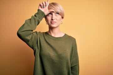 Wall Mural - Young blonde woman with modern short hair wearing casual sweater over yellow background making fun of people with fingers on forehead doing loser gesture mocking and insulting.