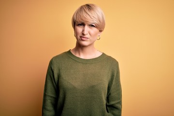 Canvas Print - Young blonde woman with modern short hair wearing casual sweater over yellow background skeptic and nervous, frowning upset because of problem. Negative person.