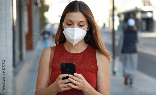 COVID-19 Pandemic Coronavirus Young Woman Wearing KN95 FFP2 Mask Using Smart Phone App in City Street to Aid Contact Tracing in Response to the 2019-20 Coronavirus Pandemic