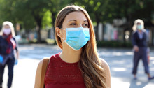 COVID-19 Social Distancing Woman In City Street Wearing Surgical Mask Against Disease Virus SARS-CoV-2. Girl With Face Mask Walks Respecting Social Distancing During Pandemic Coronavirus Disease 2019.