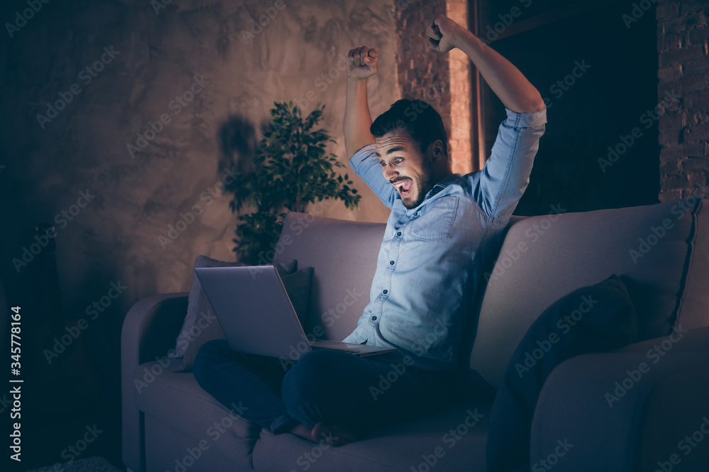 Profile side view of his he nice attractive lucky cheerful cheery glad brunet guy sitting on divan using laptop rejoicing having fun at modern loft industrial style interior dark room apartment flat - obrazy, fototapety, plakaty 
