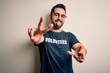 © Krakenimages.com - Handsome man with beard wearing t-shirt with volunteer message over white background smiling with tongue out showing fingers of both hands doing victory sign. Number two.