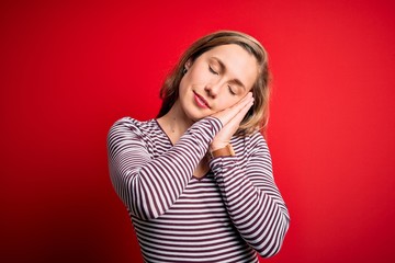 Sticker - Young beautiful blonde woman wearing casual striped t-shirt over isolated red background sleeping tired dreaming and posing with hands together while smiling with closed eyes.