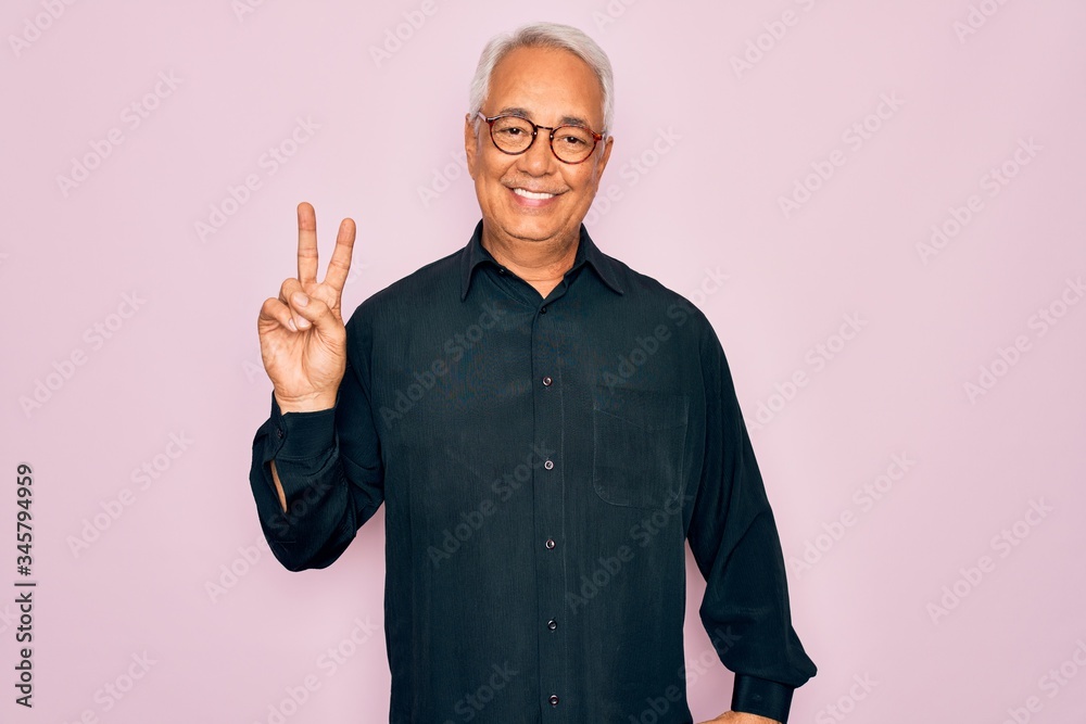 Middle age senior grey-haired handsome man wearing glasses and elegant shirt smiling with happy face winking at the camera doing victory sign. Number two.