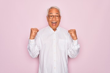 Wall Mural - Middle age senior grey-haired man wearing glasses and business shirt over pink background celebrating surprised and amazed for success with arms raised and open eyes. Winner concept.