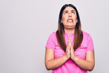 Young beautiful brunette woman wearing casual pink t-shirt standing over white background begging and praying with hands together with hope expression on face very emotional and worried. Begging.