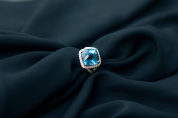 Blue gemstone diamond ring on black fabric. Jewelry product photography. 