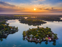 Budapest, Hungary - Aerial View Of Small Fishing Island On Lake Kavicsos (Kavicsos To) Of Csepel District With A Warm Sunrise And Reflecting Clouds. The Island Is Full With Fishing Huts And Cabins