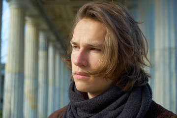 Thoughtful young man with long brown hair gazing troubled into the distance in an urban setting at sunset in winter.