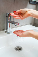 Wall Mural - White sink with a silver faucet in the bathroom. Gray can with liquid soap for hands. Turning on the tap water, personal hand hygiene. Hand washing under running water