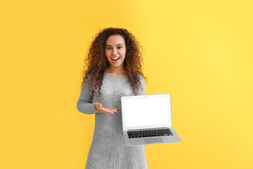 Wall Mural - Beautiful young African-American woman with laptop on color background