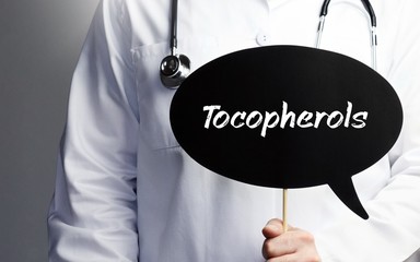 Tocopherols. Doctor in smock holds up speech bubble. The term Tocopherols is in the sign. Symbol of illness, health, medicine