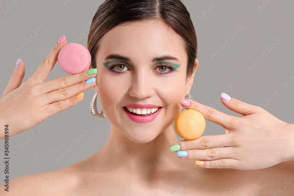 Young woman with beautiful manicure and macarons on grey background