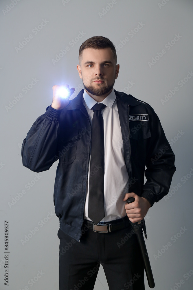 Male security guard with flashlight on grey background