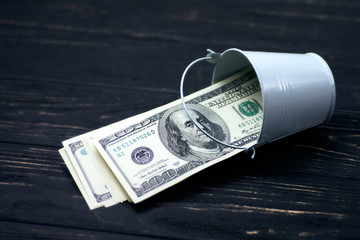 Bucket of one hundred dollars banknotes on black wooden table.