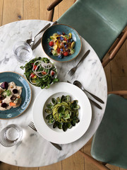 Wall Mural - Delicious lunch in a restaurant served on the marble table featuring colourful salad and seafood and green pesto spaghetti pasta