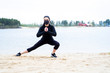 © viktoriya - a girl with dark hair and fair skin in black sportswear and a black protective mask is engaged in sports on the sand by the lake in the forest.