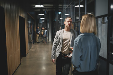 Wall Mural - Mature businessman talking with a coworker in an office hallway