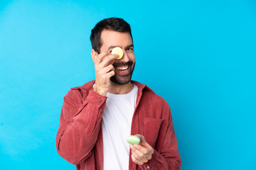 Young caucasian man over isolated blue background holding colorful French macarons