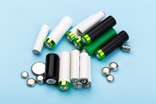 Many New And Used Batteries Of Different Shapes, AA, Round Batteries On A Blue Background.